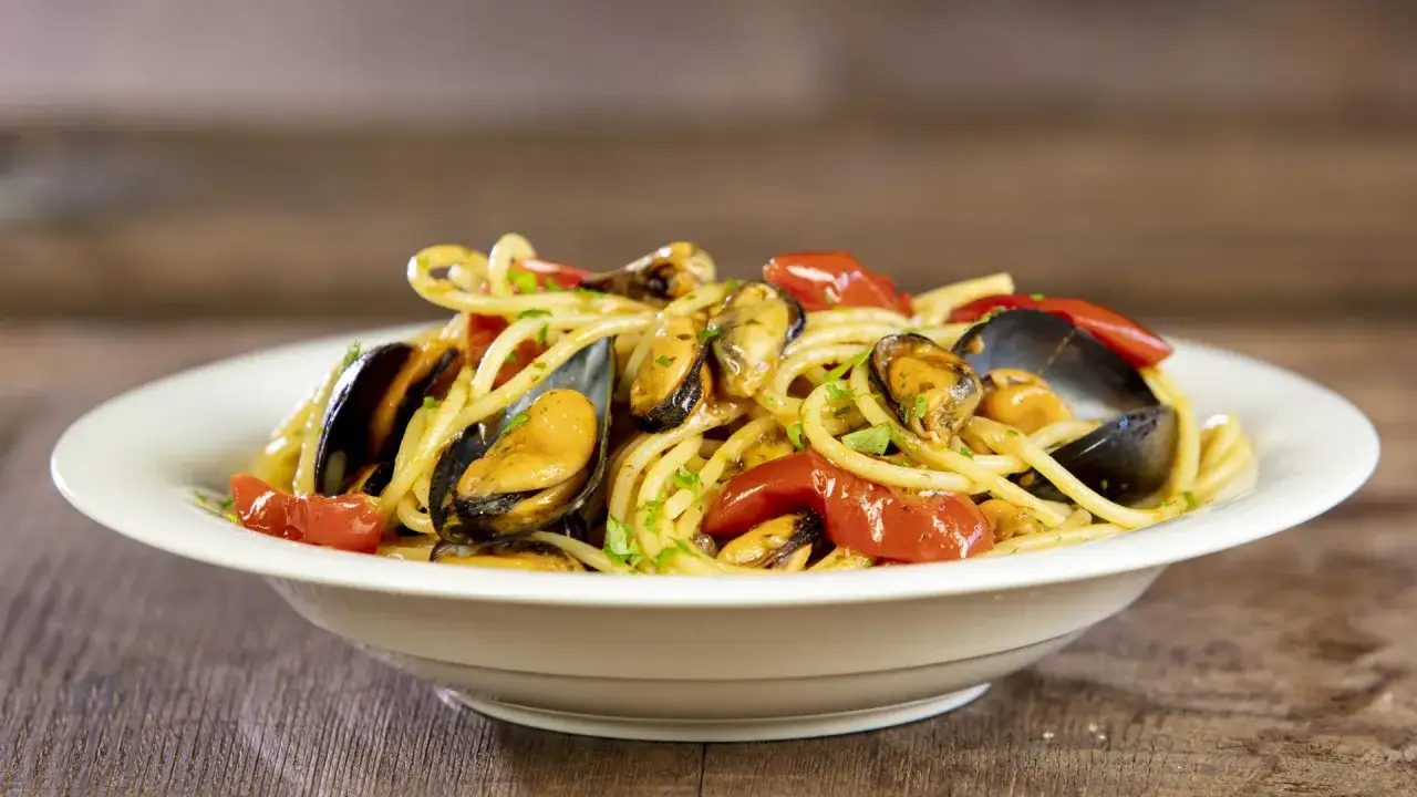 Un piatto invitante di spaghetti con le cozze, pomodorini e prezzemolo fresco su un tavolo di legno.