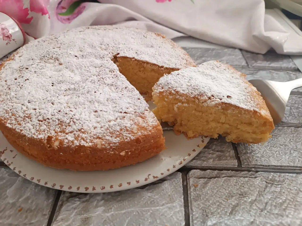 Una soffice torta al latte, cosparsa di zucchero a velo, con una fetta appena tagliata pronta per essere gustata.