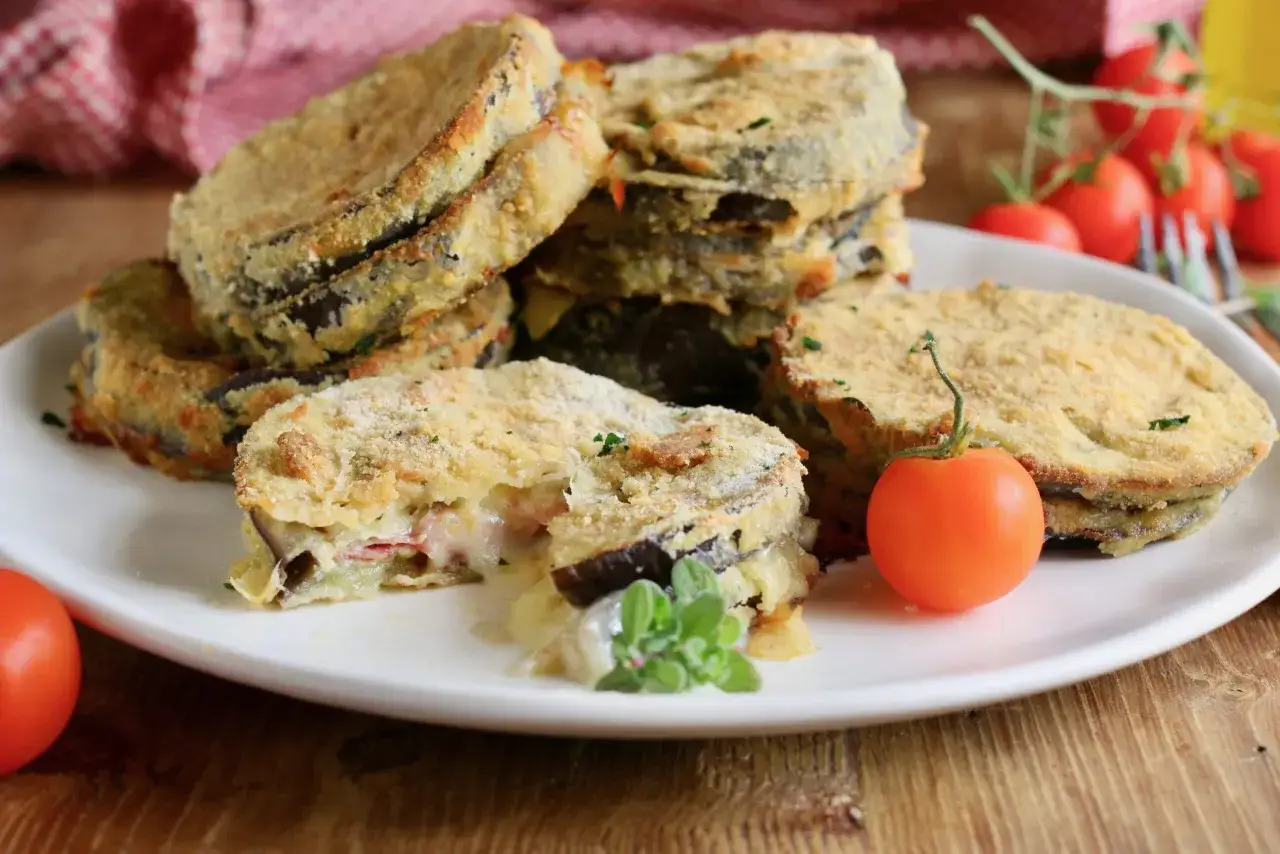 Deliziosi cordon bleu di melanzane impanati e fritti, con un ripieno filante di formaggio e prosciutto, guarniti con pomodorini freschi.