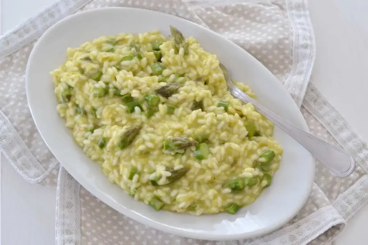 Un cremoso risotto con asparagi, servito su un piatto bianco ovale, con una forchetta appoggiata sopra.
