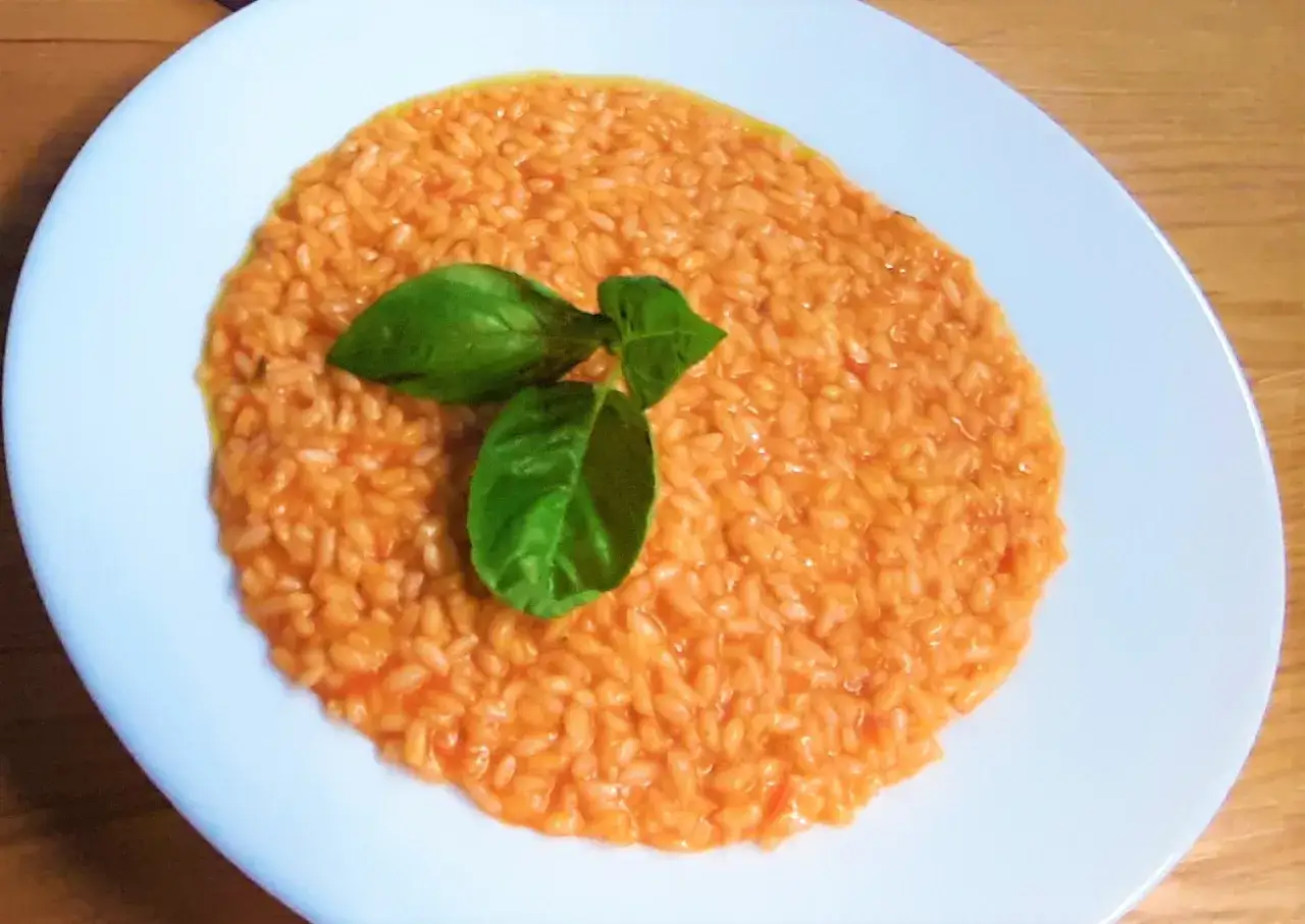 Un cremoso risotto al pomodoro, guarnito con foglie di basilico fresco, pronto per essere gustato.