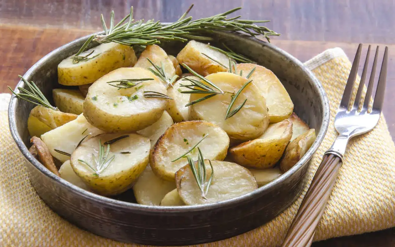 Patate novelle al forno, dorate e profumate al rosmarino, servite in una ciotola di metallo con una forchetta accanto.
