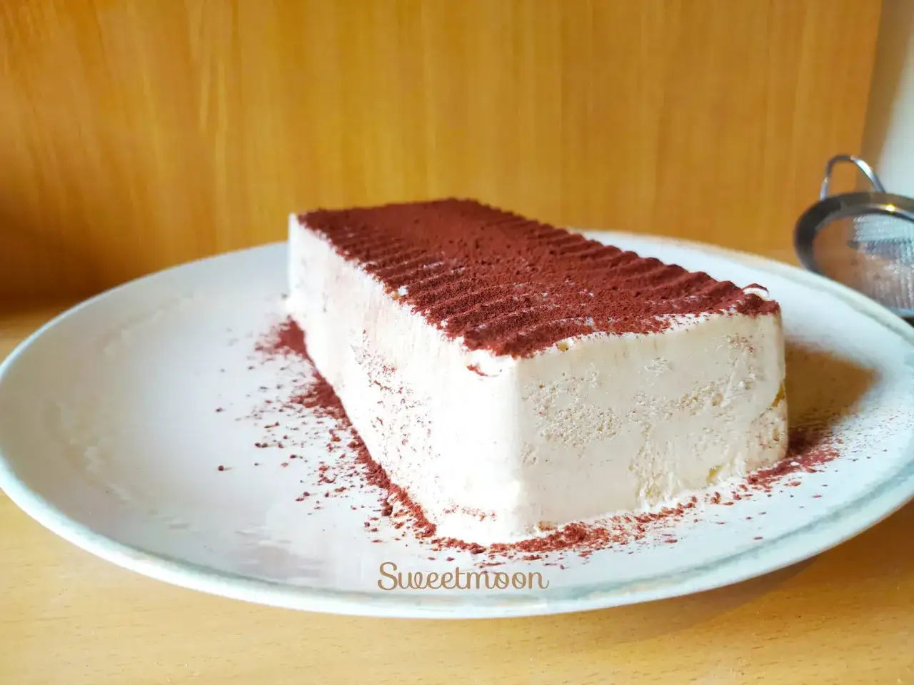 Un delizioso semifreddo al caff&egrave;, spolverato di cacao, su un piatto bianco.