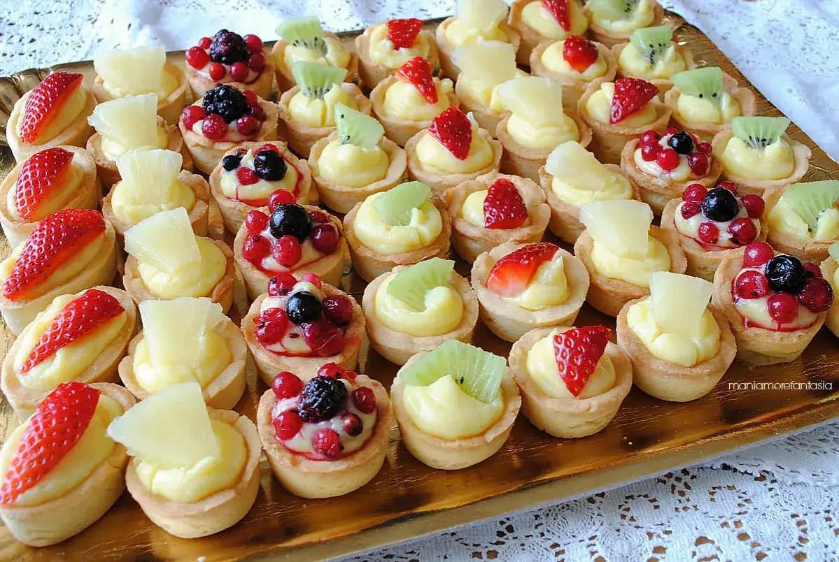 Vassoio dorato pieno di tartellette alla frutta, con fragole, kiwi, ribes e mirtilli su crema pasticcera.