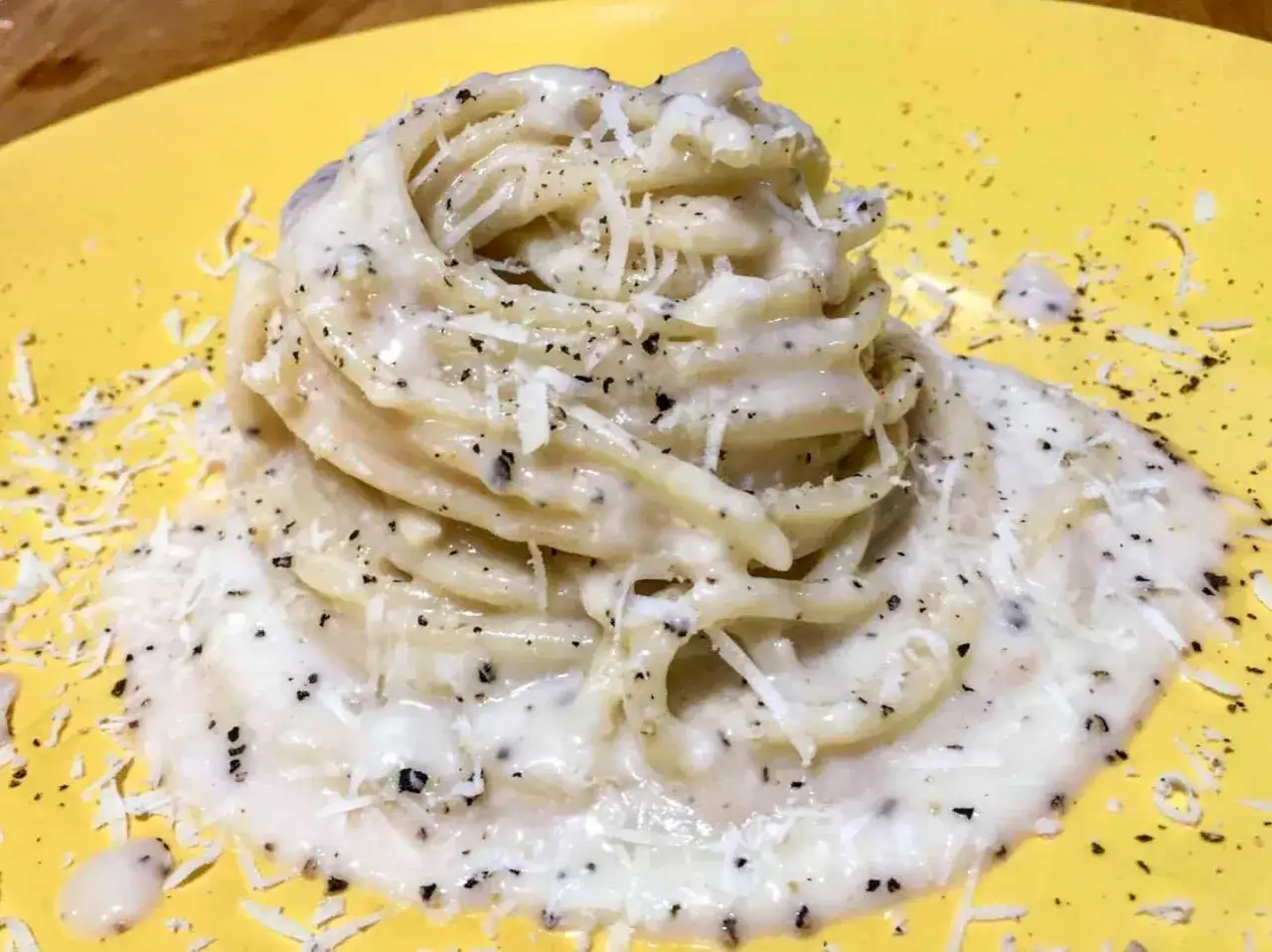 Un piatto di spaghetti cremosi, conditi con abbondante cacio e pepe, guarniti con formaggio grattugiato e pepe nero macinato.