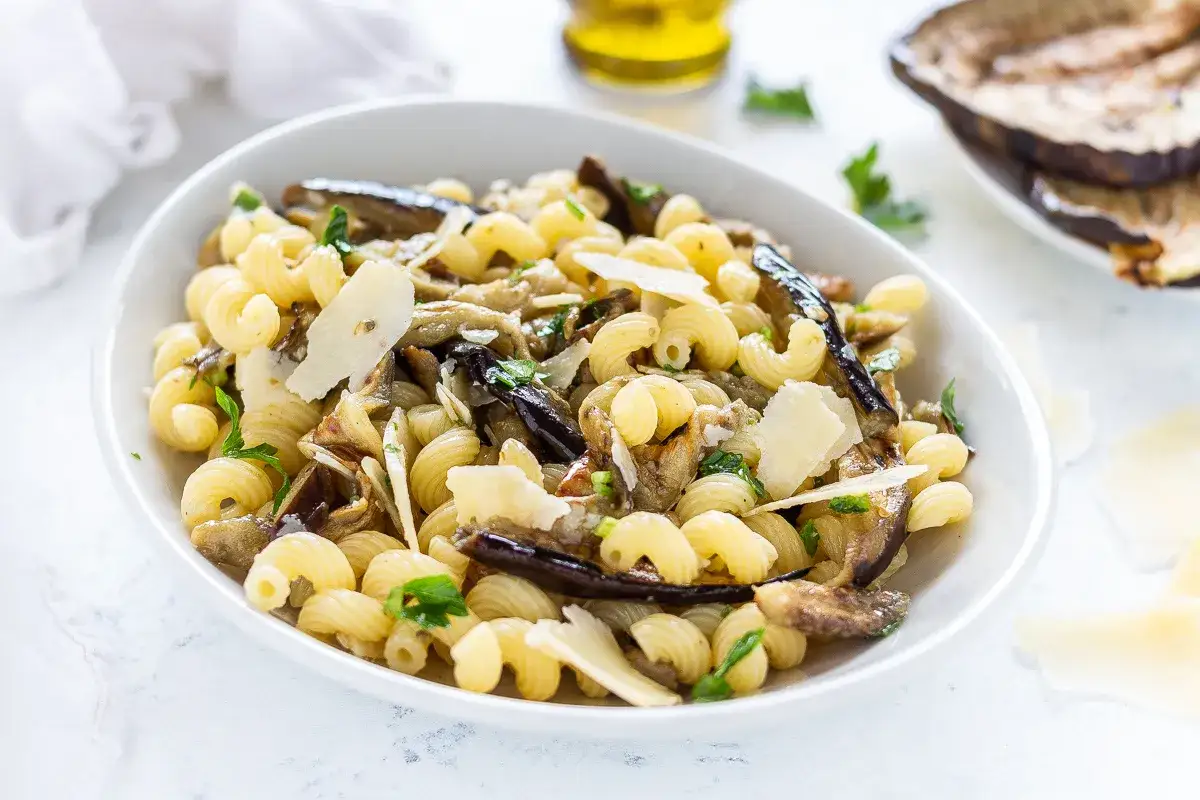 Piatto di pasta con melanzane in bianco, condita con scaglie di parmigiano e prezzemolo fresco.