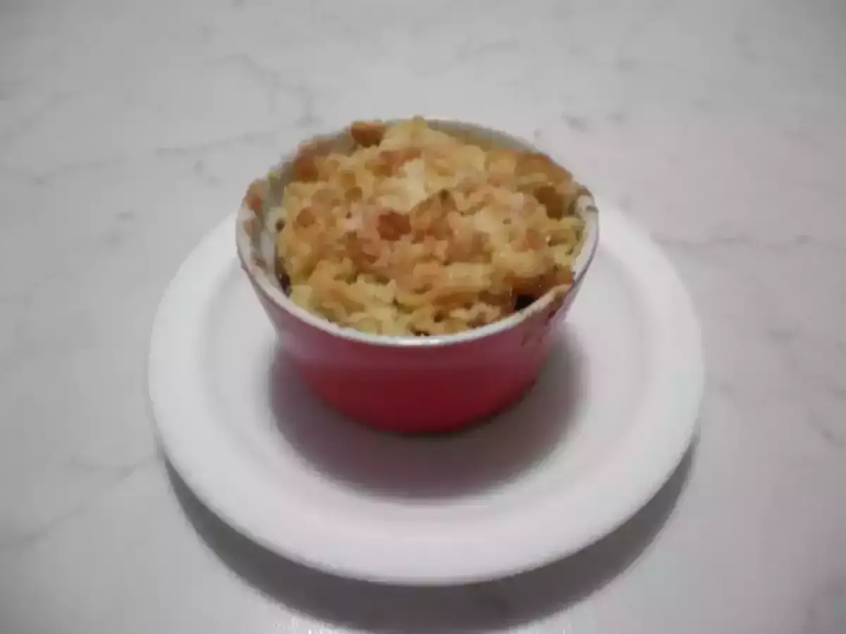 Un delizioso crumble di mele appena sfornato, servito in una ciotola rossa su un piatto bianco.