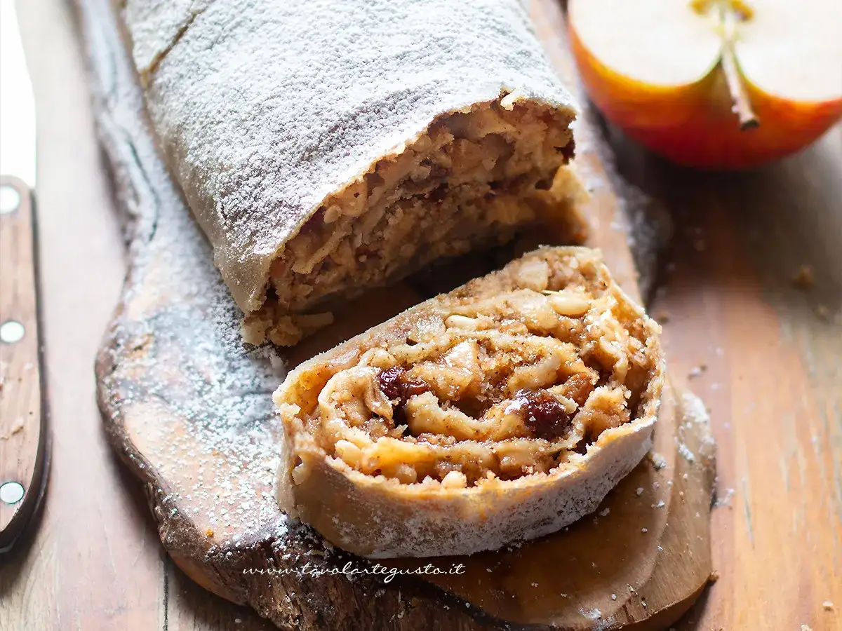 Delizioso strudel di mele con pasta sfoglia, cosparso di zucchero a velo, su un tagliere di legno.