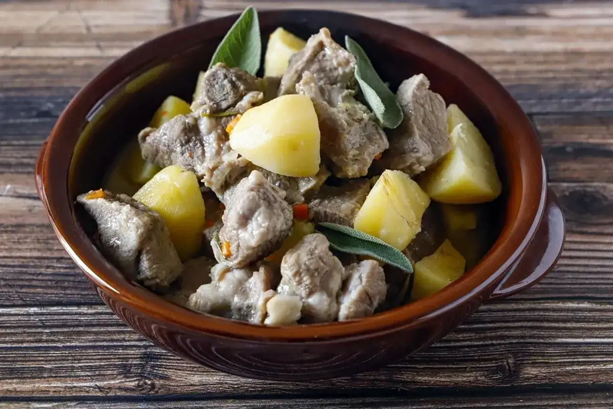 Spezzatino con patate e salvia in ciotola di terracotta, un piatto rustico e saporito.