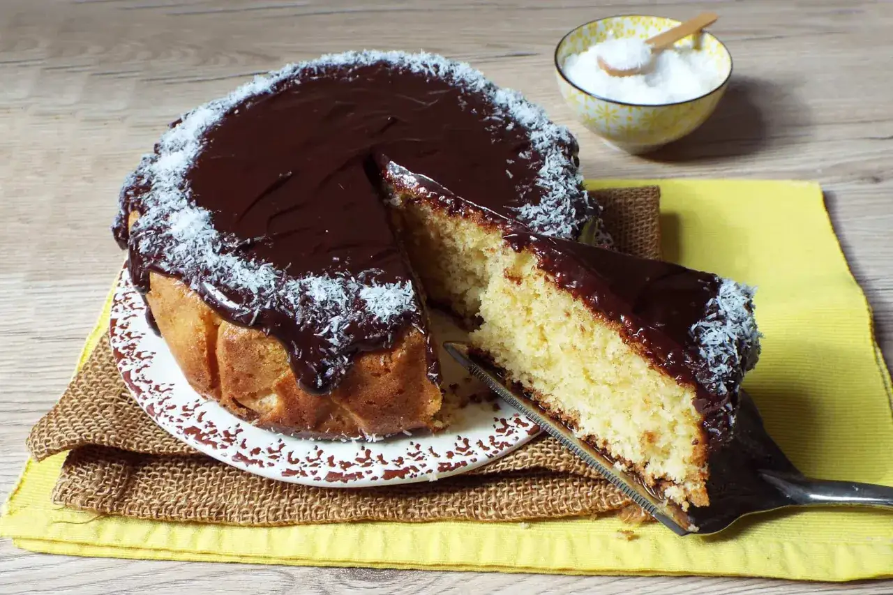 Una fetta di torta cocco e cioccolato, con glassa lucida e cocco grattugiato, pronta per essere gustata.