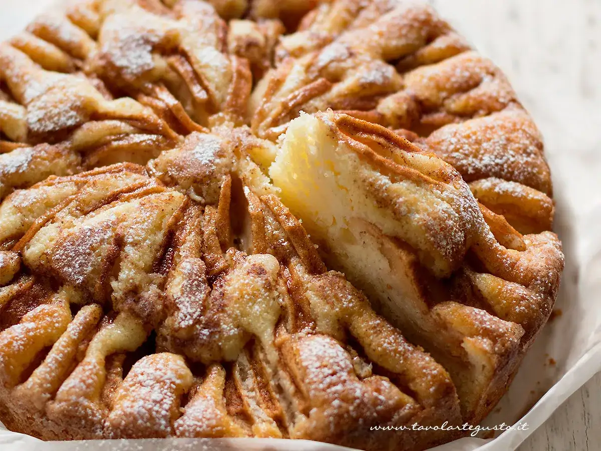 Una fetta di torta di mele, cosparsa di zucchero a velo, che sembra la torta di mele più buona che abbia mai mangiato.