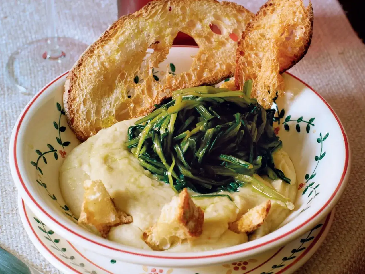 Fave e cicoria in ciotola decorata, con crostini di pane abbrustolito.