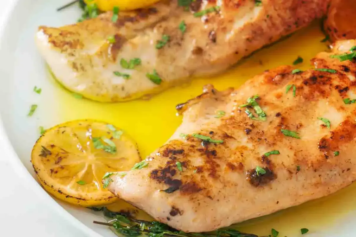 Delizioso petto di pollo dorato, servito con fette di limone e erbe aromatiche in un succo dorato.