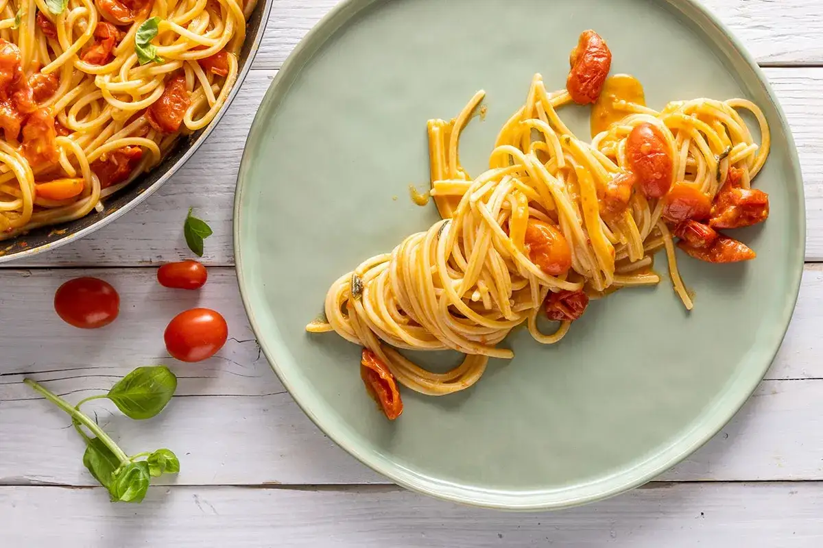 Un piatto di spaghetti allo scarpariello, conditi con pomodorini freschi e basilico, serviti su un piatto verde chiaro.