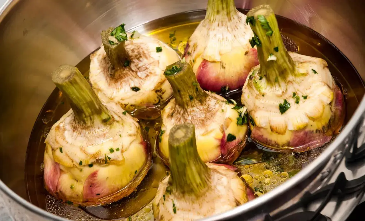 Carciofi alla romana ricetta: carciofi interi preparati in padella con erbe aromatiche, pronti per essere cotti.