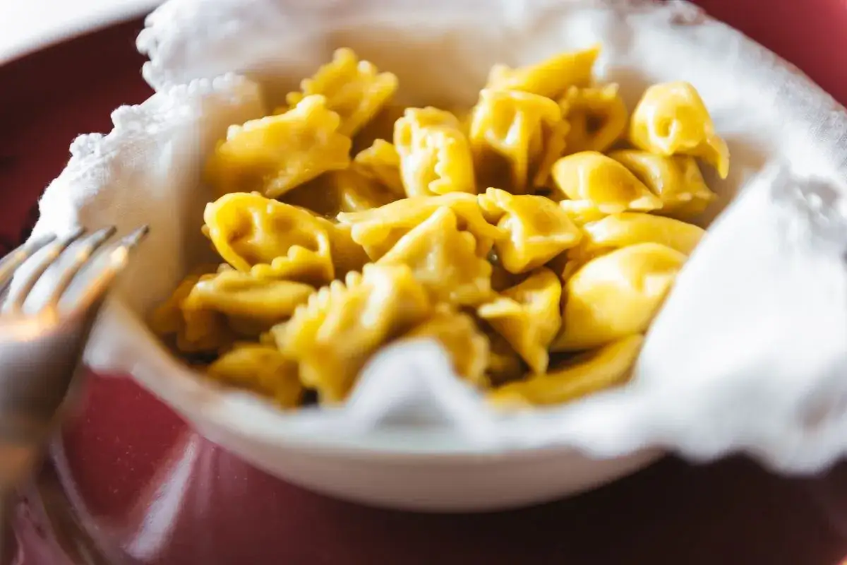 Un primo piatto invitante: ravioli del plin dorati, serviti in una ciotola con un tovagliolo bianco.