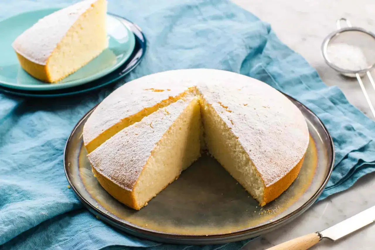 Torta soffice spolverata di zucchero a velo, un'idea per dolci con albumi veloci. Una fetta è già servita su un piattino.