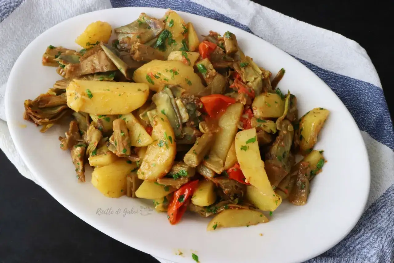 Piatto di carciofi e patate in padella, conditi con erbe aromatiche e pomodorini. Un contorno saporito e colorato.