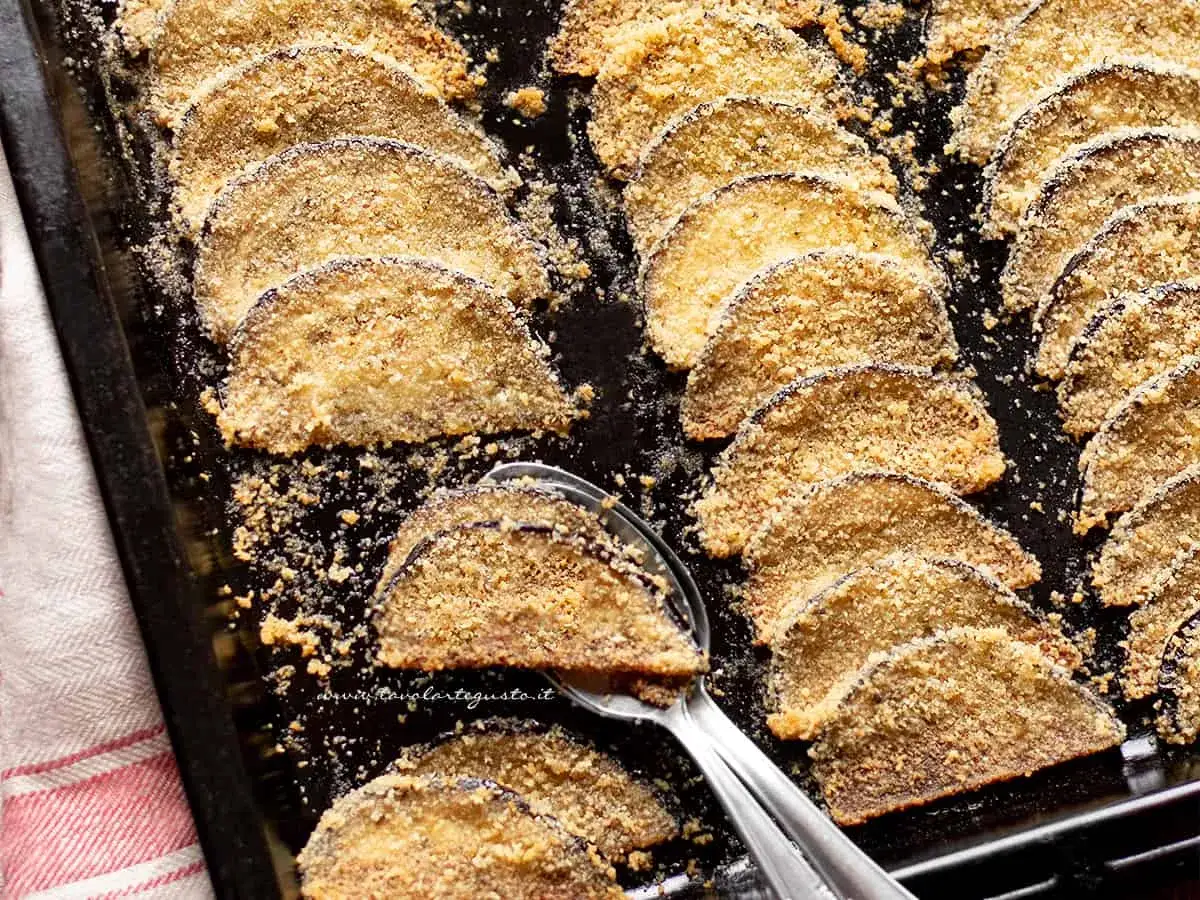 Fette di melanzane al forno dorate e croccanti, disposte su una teglia, pronte per essere gustate.