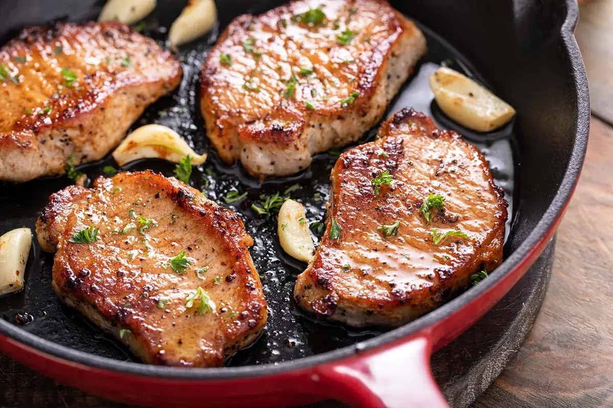 Quattro succulente lonze di maiale in padella, dorate e profumate con aglio e prezzemolo.