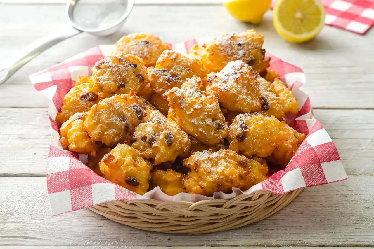 Frittelle di riso ricetta della nonna: dolcetti dorati e soffici, cosparsi di zucchero a velo, in un cestino foderato con tovagliolo a quadri rossi.