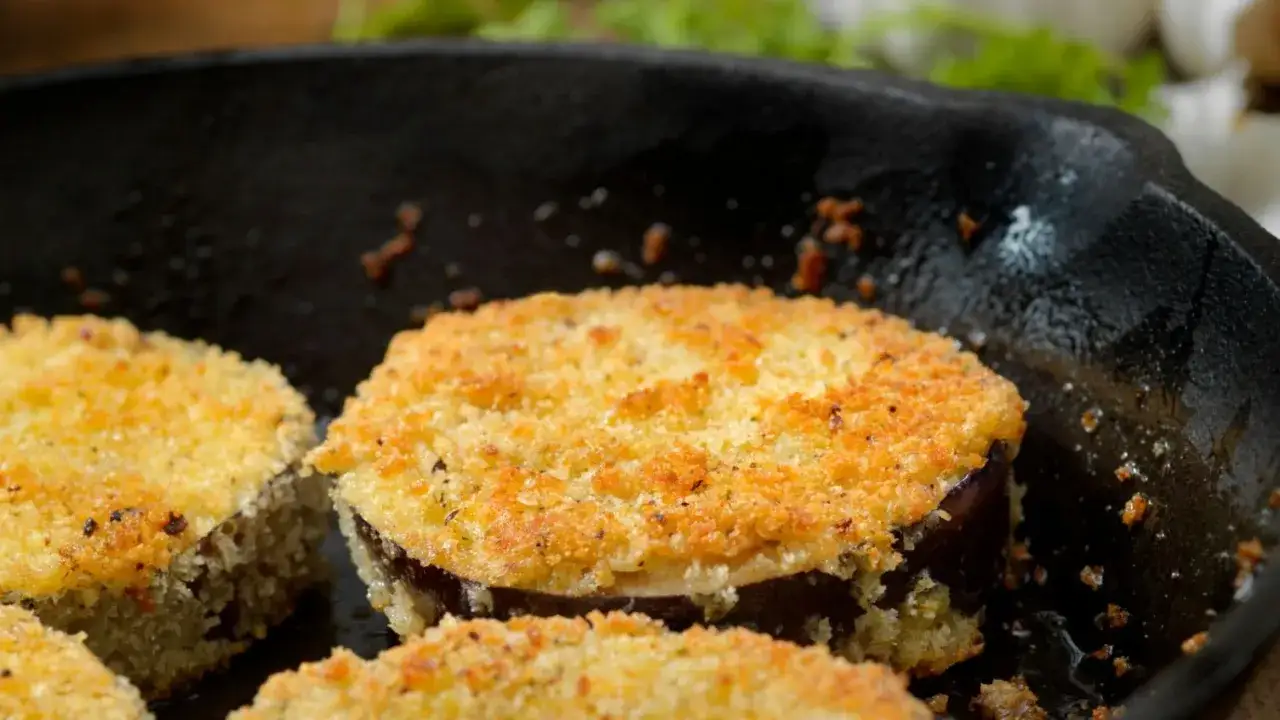 Fette di melanzane in padella, dorate e croccanti grazie al pangrattato, pronte per essere gustate.