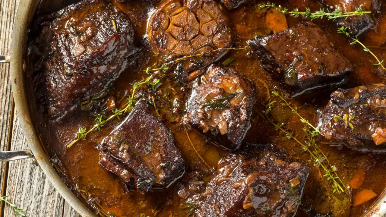 Succulento brasato di manzo cotto lentamente in una ricca salsa, guarnito con erbe aromatiche fresche e spicchi d'aglio caramellati.