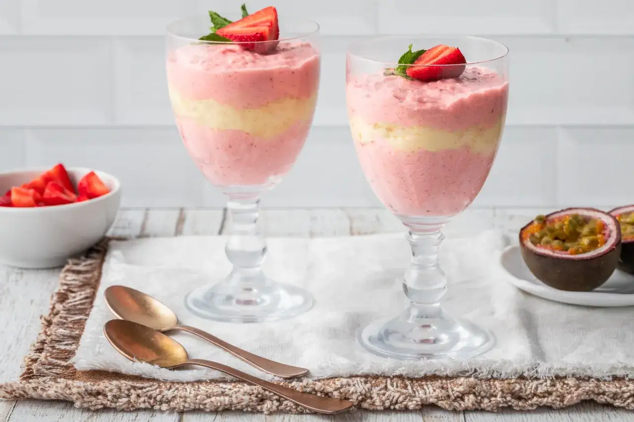 Deliziosa bavarese alle fragole a strati, guarnita con fragole fresche e menta. Accanto, una ciotola di fragole e frutti della passione.