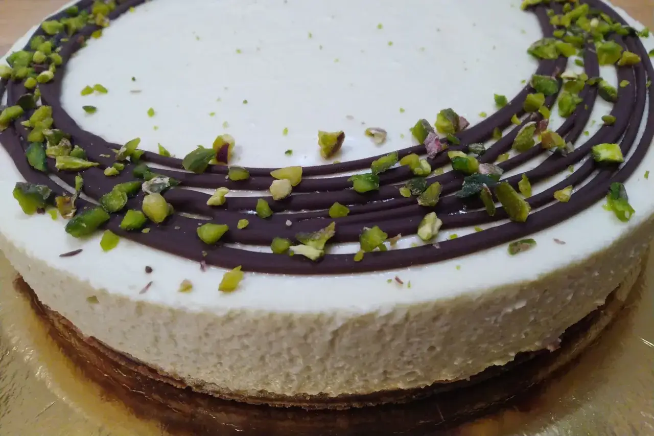 Delizioso cheesecake al pistacchio con decorazioni di cioccolato fondente e granella verde brillante.