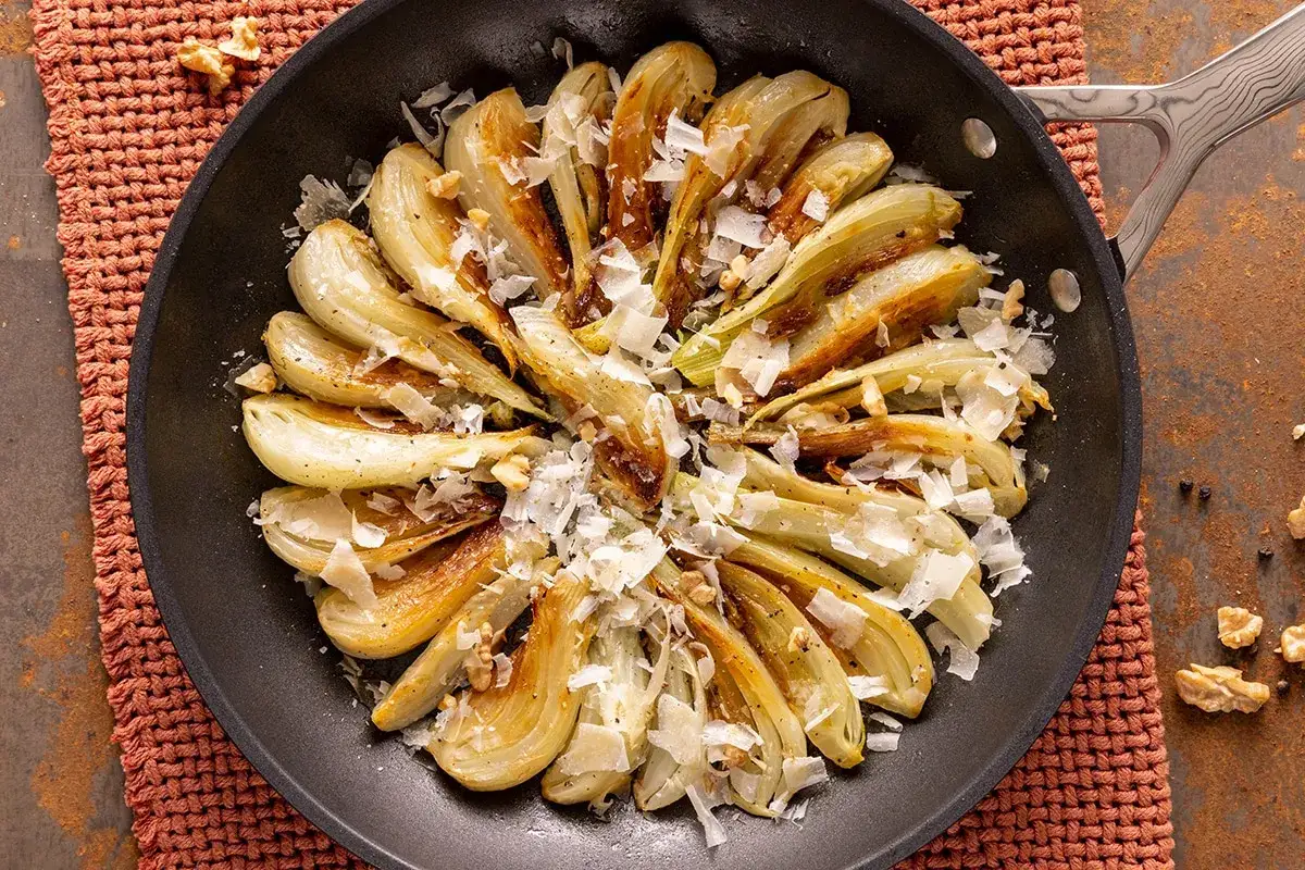 Finoçchi gratinati in padella, dorati e saporiti, guarniti con scaglie di formaggio e noci croccanti.