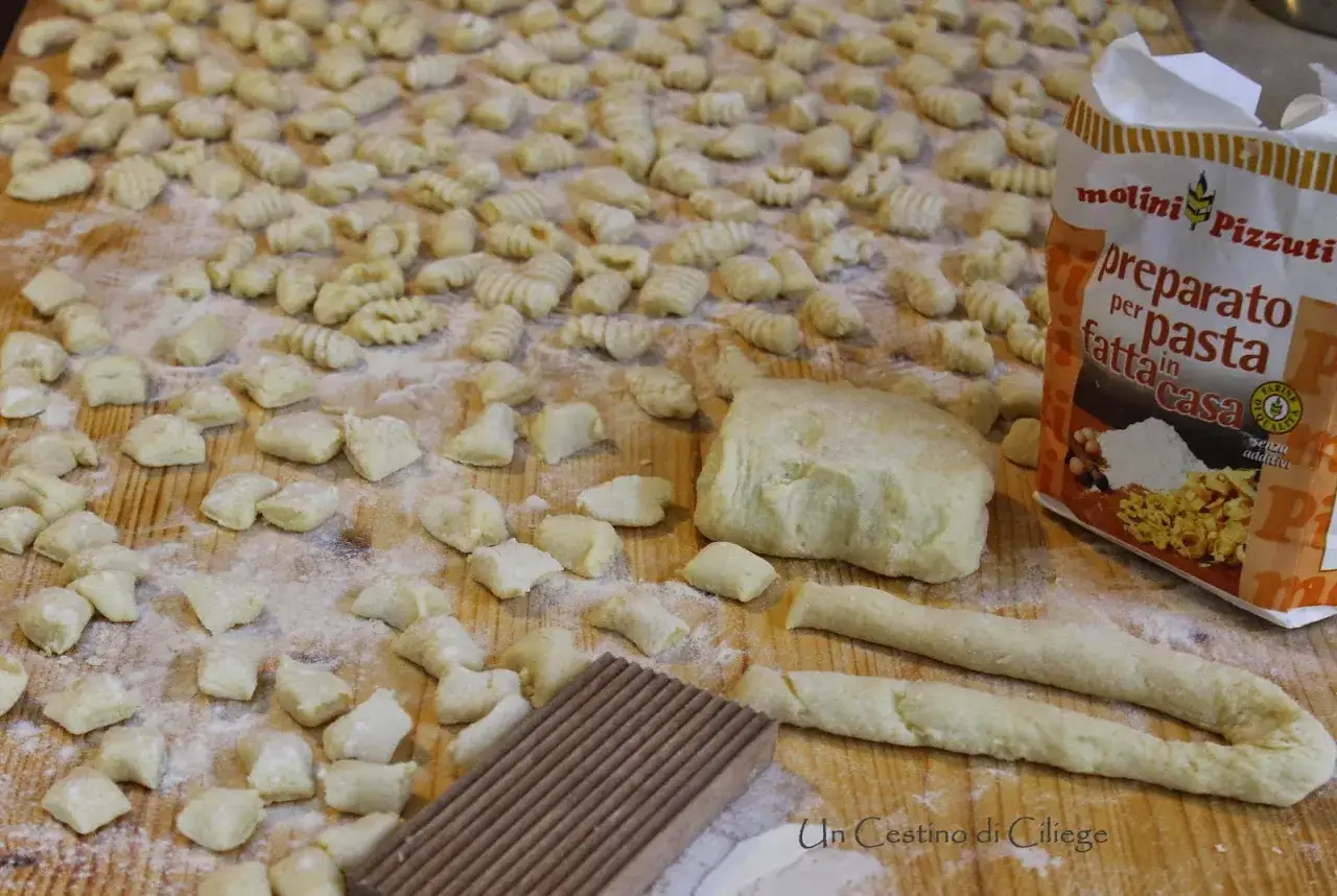 Tanti gnocchi di patate fatti in casa, alcuni gi&agrave; formati, altri in lavorazione su un tagliere infarinato. Accanto, un impasto e una confezione di preparato per pasta.