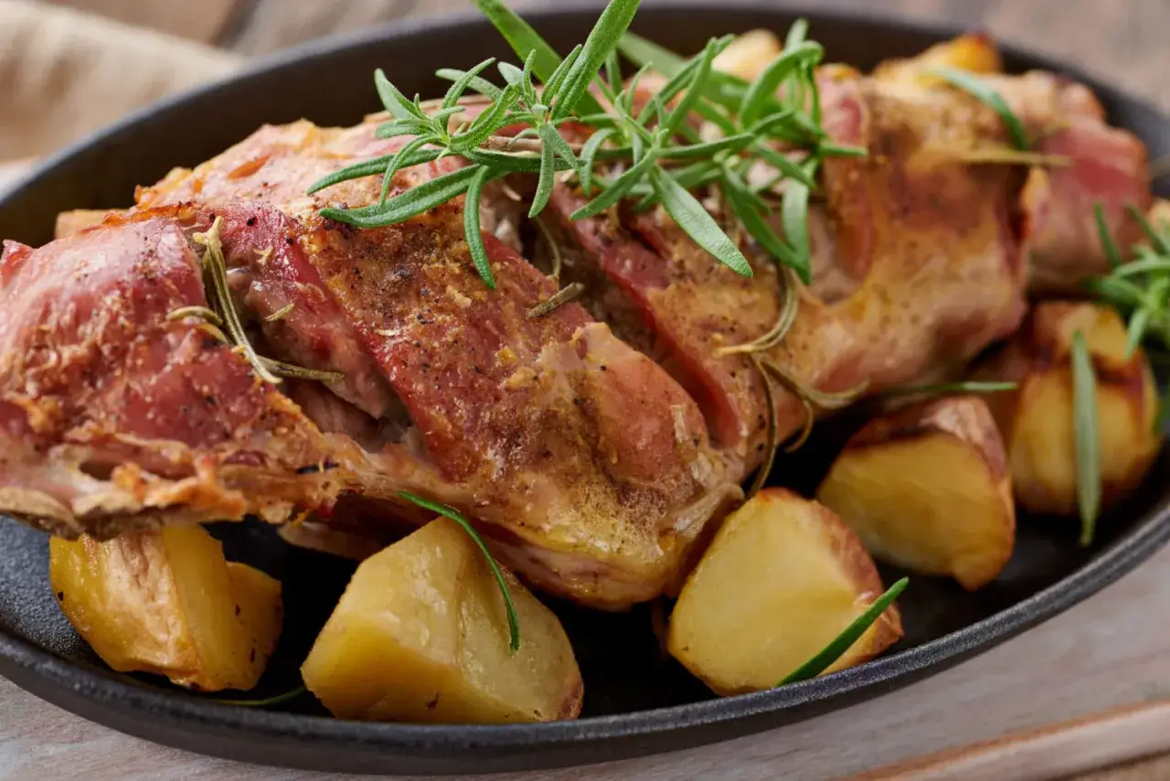 Succulento agnello al forno, dorato e profumato al rosmarino, servito con patate arrosto in una padella di ghisa.
