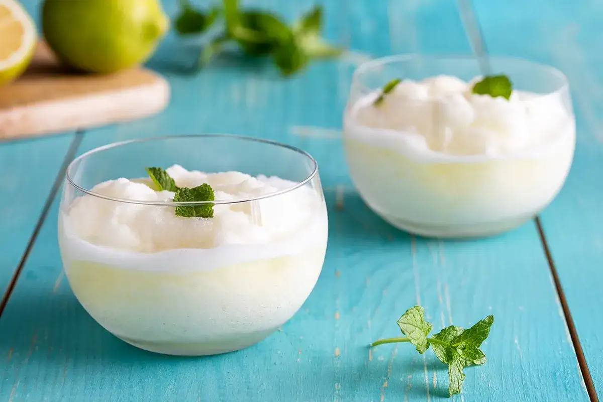 Due bicchieri di sorbetto al limone senza albume, guarniti con menta fresca, su un tavolo di legno blu.