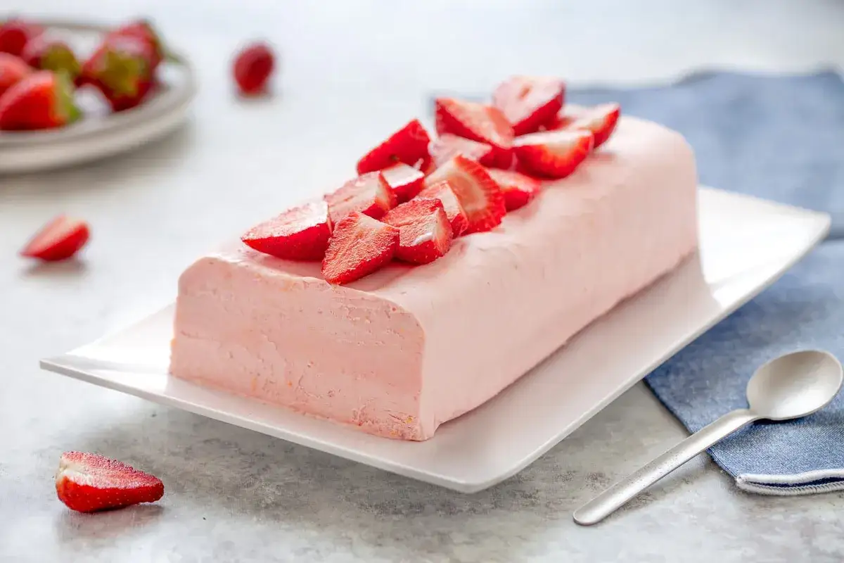 Delizioso semifreddo alle fragole, guarnito con fragole fresche, su un piatto bianco.