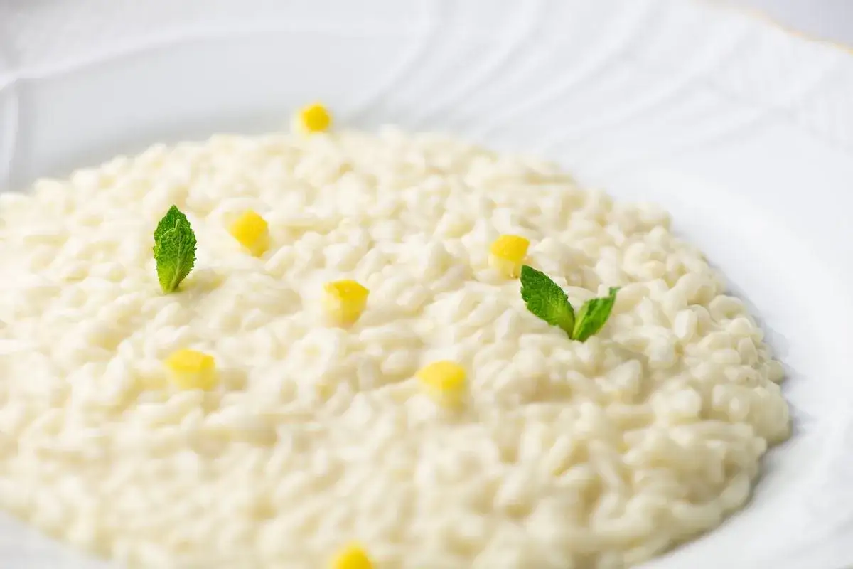 Un cremoso risotto al limone, guarnito con cubetti di limone e foglie di menta fresca, pronto per essere gustato.