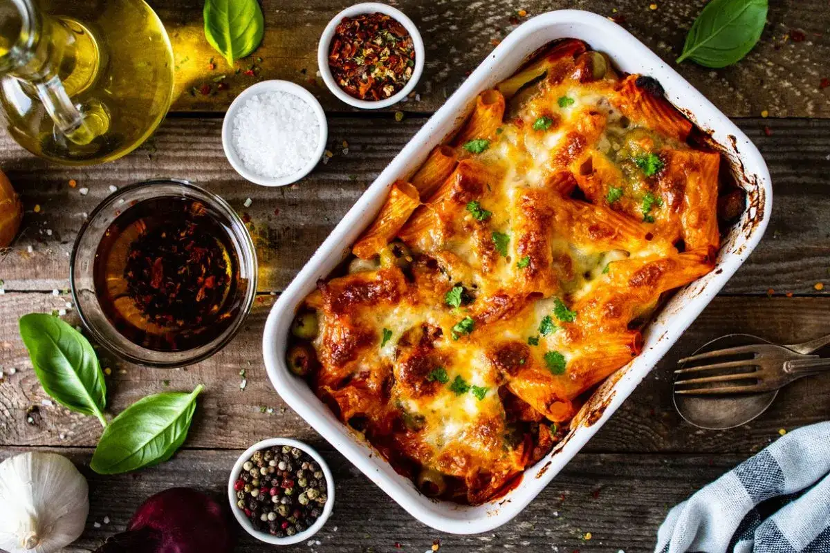 Piatto fumante di pasta pasticciata al forno, con formaggio fuso e erbe aromatiche, pronto per essere gustato.