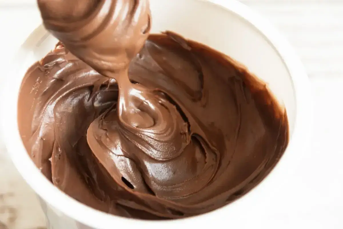 Crema al cioccolato densa e lucida, con onde morbide create da un cucchiaio che la preleva.