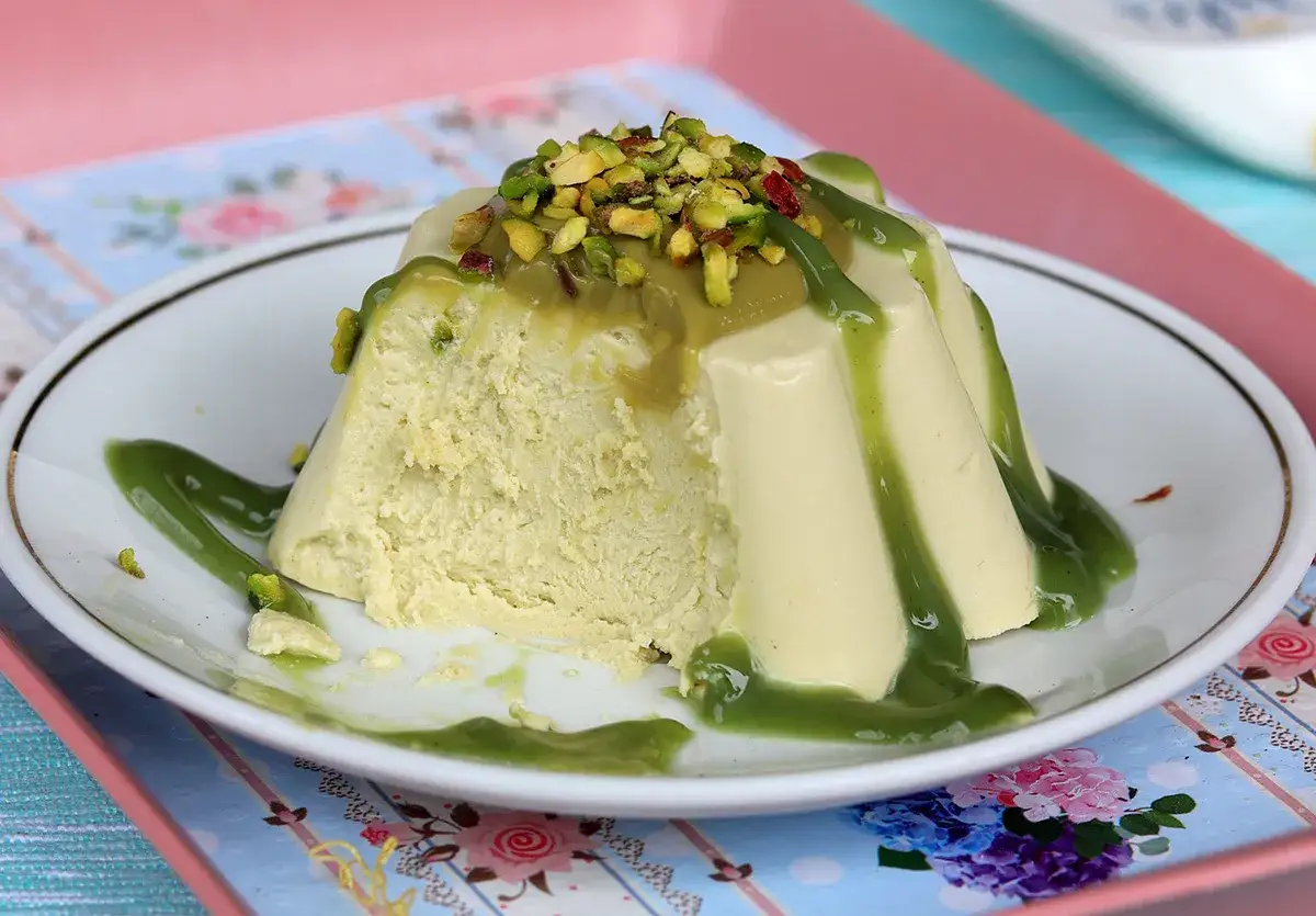 Delizioso semifreddo al pistacchio, guarnito con granella di pistacchi e salsa verde, servito su un piatto bianco con un motivo floreale.
