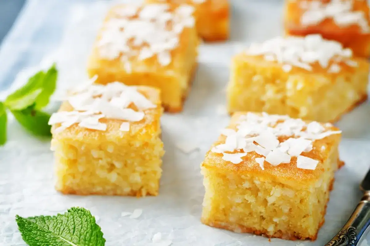 Deliziosi quadretti di torta al cocco, guarniti con scaglie di cocco e foglioline di menta fresca.