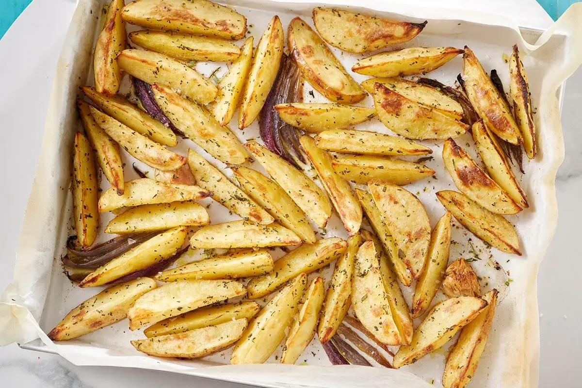 Patate al forno dorate e croccanti, condite con erbe aromatiche, su una teglia foderata di carta forno.