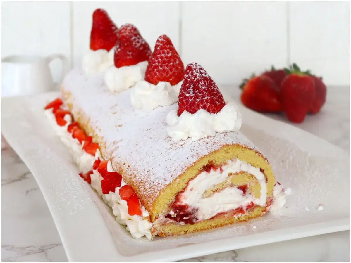 Rotolo panna e fragole, soffice e decorato con panna montata e fragole fresche, spolverato di zucchero a velo.