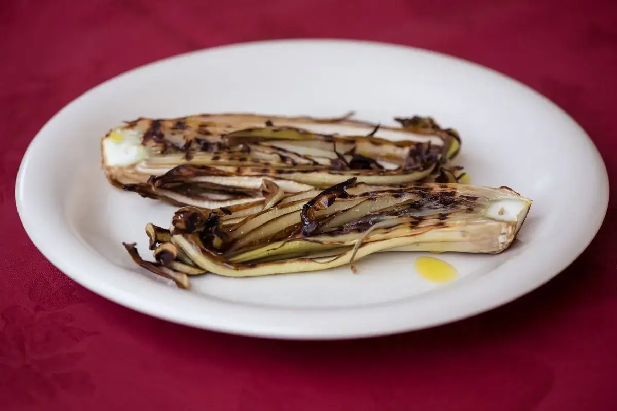 Radicchio in padella, grigliato e condito con olio d'oliva, servito su un piatto bianco.