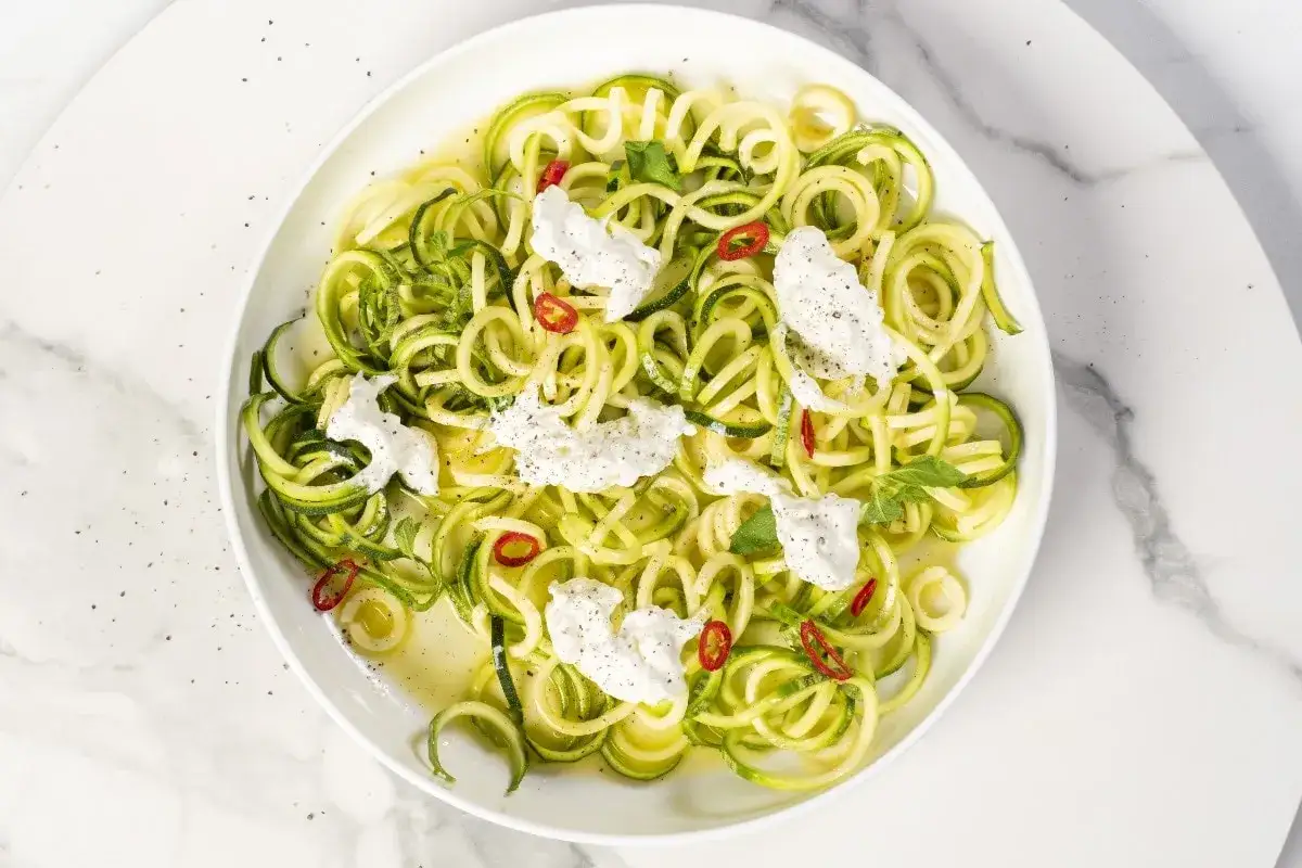 Un piatto di spaghetti di zucchine freschi, conditi con ricotta cremosa, peperoncino e erbe aromatiche.