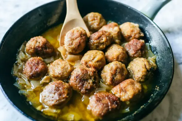 Polpette in bianco cremose in padella, dorate e succulente, adagiate su un letto di cipolle caramellate.