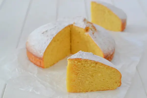 A fluffy lemon cake dusted with powdered sugar, with two slices cut out.