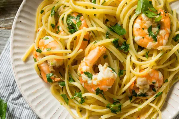 Un piatto invitante di pasta con gamberetti, condita con prezzemolo fresco e servita su un piatto bianco.