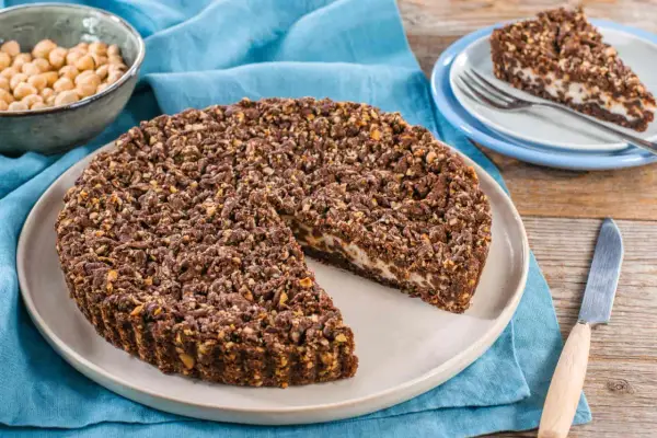 Sbriciolata ricotta e cioccolato con croccante copertura di nocciole. Una fetta è già servita su un piattino.