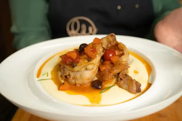 Pollo alla cacciatora ricetta della nonna: succulenti pezzi di pollo in umido con pomodoro, olive e carote, serviti su un letto di polenta cremosa.