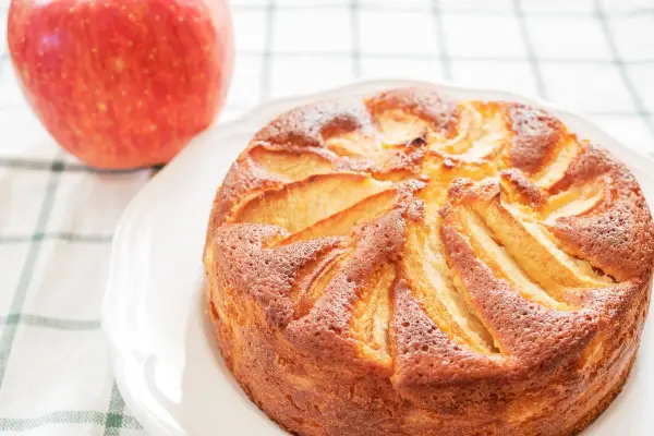 Torta di mele con yogurt, dorata e soffice, con mele a vista. Accanto, una mela rossa fresca.