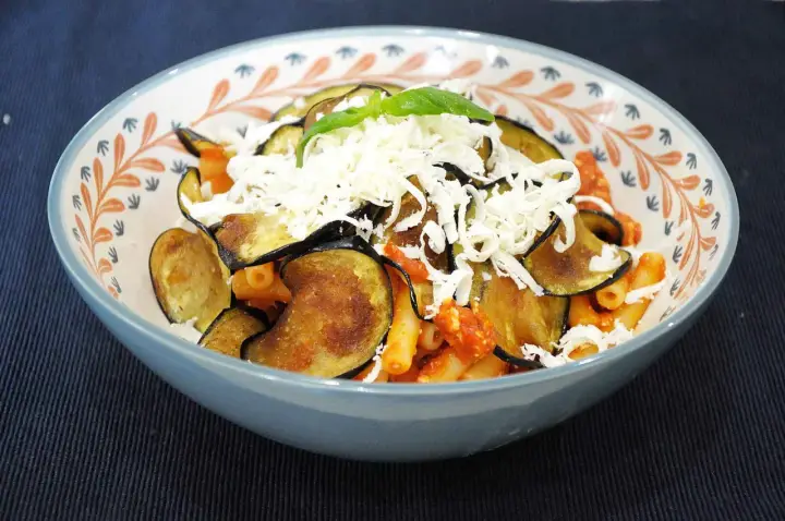 Un piatto di pasta alla norma fumante, con melanzane fritte, sugo rosso e abbondante ricotta salata grattugiata.
